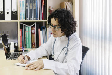 Ärztin beim Schreiben am Laptop, sitzend am Schreibtisch im Büro - XLGF00252