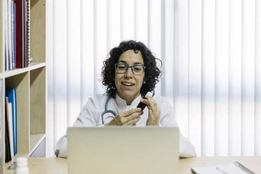 Smiling female doctor discussing medicine through video call on laptop in office - XLGF00253