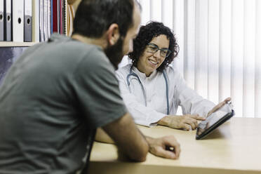 Eine lächelnde Ärztin zeigt einem Patienten in einer Klinik ein digitales Tablet - XLGF00261