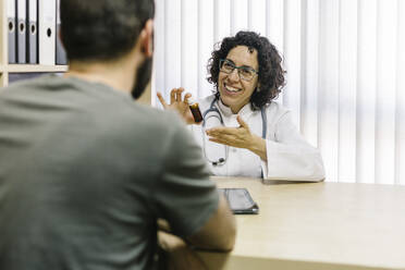 Lächelnde Ärztin, die mit einem Patienten im Büro in einer Klinik über Medikamente diskutiert - XLGF00262
