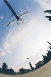 Fish-eye view of teenage girl playing basketball against sky - GIOF08422