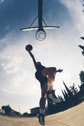 Low angle view of female athlete jumping while dunking basketball against sky - GIOF08423