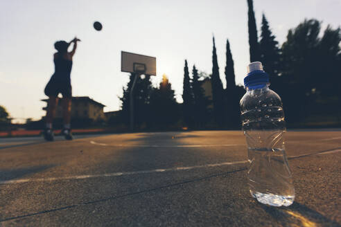 Nahaufnahme einer Wasserflasche in der Nähe einer Basketballspielerin, die auf dem Platz übt - GIOF08425