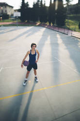 Teenage basketball player standing with ball on court - GIOF08426