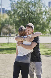 Ein sich umarmendes Paar vor dem Training im Park - JNDF00174