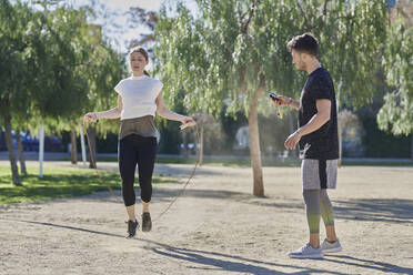 Frau beim Training mit Trainer, der im Park Seil springt - JNDF00182