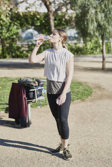 Frau trinkt Wasser während eines Workouts im Park - JNDF00187