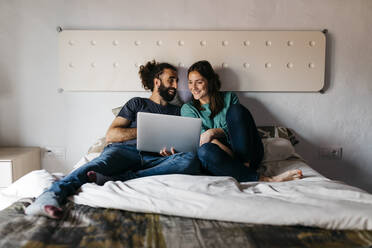 Pärchen beim Filmschauen auf dem Bett sitzend zu Hause - JRFF04537