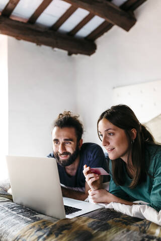 Happy couple lying on bed shopping online stock photo