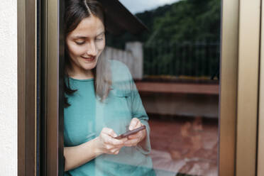 Woman using smartphone at window, man using laptop lying on bed at home - JRFF04550