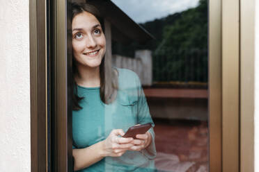 Frau mit Smartphone am Fenster, Mann mit Laptop zu Hause auf dem Bett liegend - JRFF04551