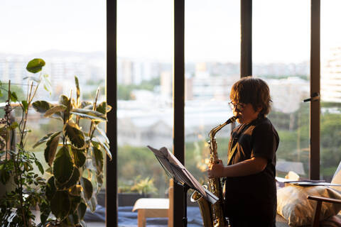 Junge übt abends zu Hause das Saxophonspielen, lizenzfreies Stockfoto
