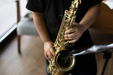 Crop-Ansicht eines Jungen, der zu Hause Saxophon spielen übt - VABF03092