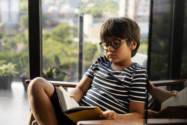 Portrait of boy reading book at home - VABF03093