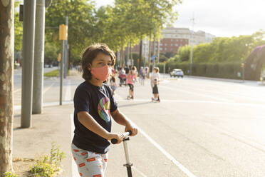 Porträt eines Jungen mit Schutzmaske auf einem Motorroller in der Stadt - VABF03095