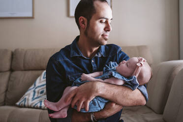 Father carrying sleeping baby girl on sofa at home - EBBF00204