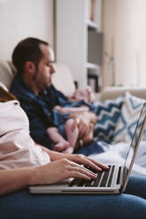 Mother using laptop while father carrying daughter in background - EBBF00207