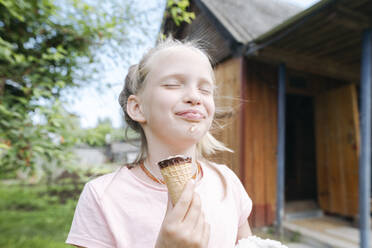 Portrait of happy blond girl with eyes closed enjoying ice cream with in garden - EYAF01170
