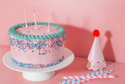 Cake stand with strawberry birthday cake, drinking straws and party hats - SKCF00633