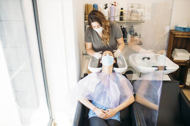 Woman with mask getting hair washed in hair salon - GMLF00252