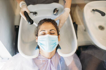 Woman with mask getting hair washed in hair salon - GMLF00253