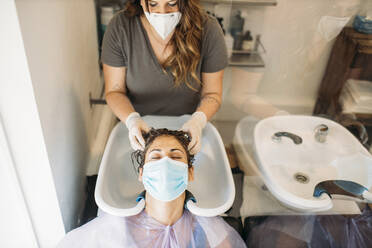 Woman with mask getting hair washed in hair salon - GMLF00254