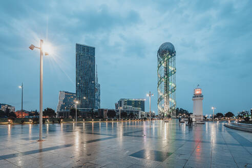 Georgia, Adjara, Batumi, Illuminated town square at dusk with Batumi Lighthouse and Alphabetic Tower in background - WVF01798