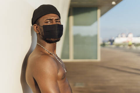 Junger Mann ohne Hemd mit Gesichtsmaske an der Wand während des Coronavirus, lizenzfreies Stockfoto