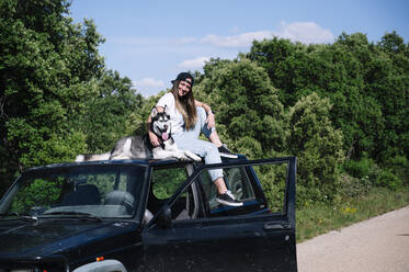 Lächelnde Frau mit Hund auf dem Dach sitzend an einem sonnigen Tag - JCMF00888