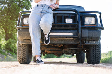 Woman leaning on vehicle hood during road trip - JCMF00896