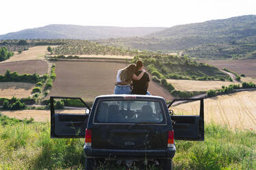 Mid adult couple sitting on 4x4 vehicle roof while looking at landscape during road trip - JCMF00907