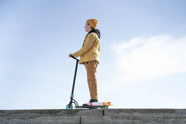 Nachdenklicher Junge mit Tretroller auf Stufen gegen blauen Himmel stehend - VPIF02529