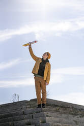 Junge hält Raketenspielzeug, während er auf Stufen gegen den Himmel steht - VPIF02532