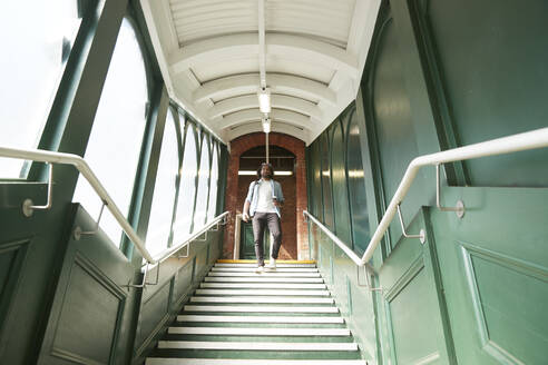 Junger trendiger Mann, der die Treppe am Bahnhof hinuntergeht - PMF01104