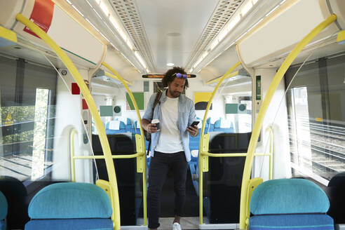 Junger trendiger Mann, der im Zug stehend ein Smartphone benutzt - PMF01110