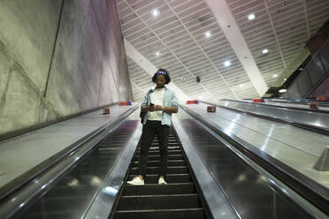 Junger trendiger Mann benutzt Smartphone auf Rolltreppe in U-Bahn-Station - PMF01112