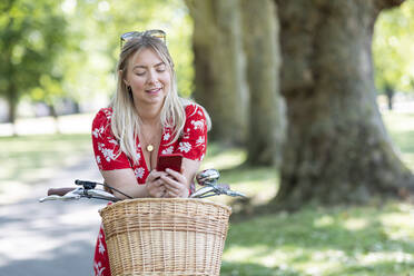 Frau benutzt Smartphone, während sie sich in einem öffentlichen Park auf ein Fahrrad stützt - WPEF03042
