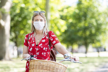 Frau mit Maske, während sie mit dem Fahrrad in einem öffentlichen Park steht - WPEF03057