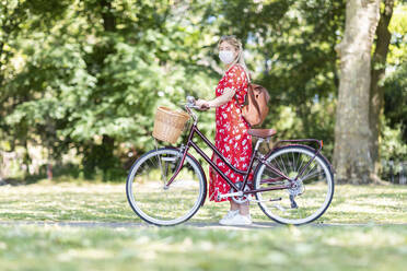 Frau mit Maske, die mit dem Fahrrad auf dem Fußweg im Park steht - WPEF03060