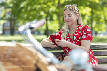 Schöne Frau, die ein Smartphone benutzt, während sie auf einer Parkbank sitzt - WPEF03062