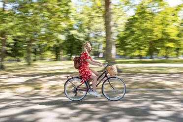 Blurred motion of woman riding bicycle on footpath at public park - WPEF03064