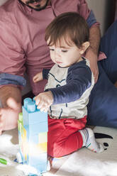 Kleiner Junge und Vater spielen zu Hause mit einem Plastikblock - FLMF00251