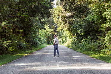 Young man standing on road amidst trees in forest - WVF01819