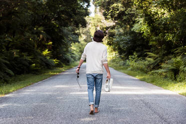 Mann mit Sportschuhen und Sonnenbrille beim Spaziergang auf der Straße inmitten von Bäumen - WVF01832