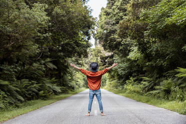 Man standing with arms outstretched on country road amidst trees in forest - WVF01836