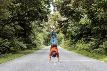 Junger Mann macht Handstand auf der Straße inmitten von Bäumen im Wald - WVF01838