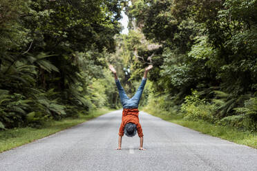 Junger Mann macht Handstand auf der Straße inmitten von Bäumen - WVF01839