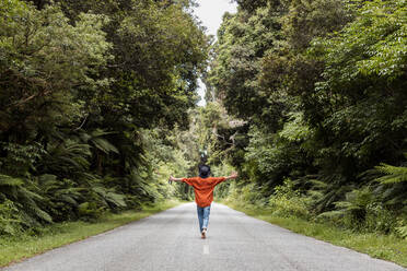 Young man walking with arms outstretched on country road in forest - WVF01843