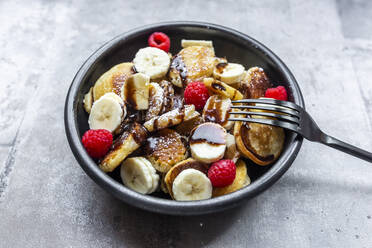 Bowl of homemade mini pancakes with bananas, raspberries, chocolate sauce and powdered sugar - SARF04602