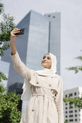 Muslimisches Teenager-Mädchen nimmt Selfie durch Smartphone in der Stadt während des sonnigen Tages - JCZF00142